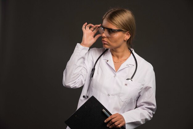 Doctora rubia con un estetoscopio usando anteojos y sosteniendo un talonario de recibos