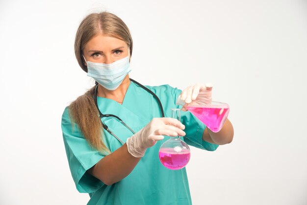 Doctora rubia con mascarilla y poniendo productos químicos de un frasco a otro.