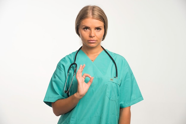 Doctora rubia en uniforme azul con estetoscopio en el cuello hace una buena señal.