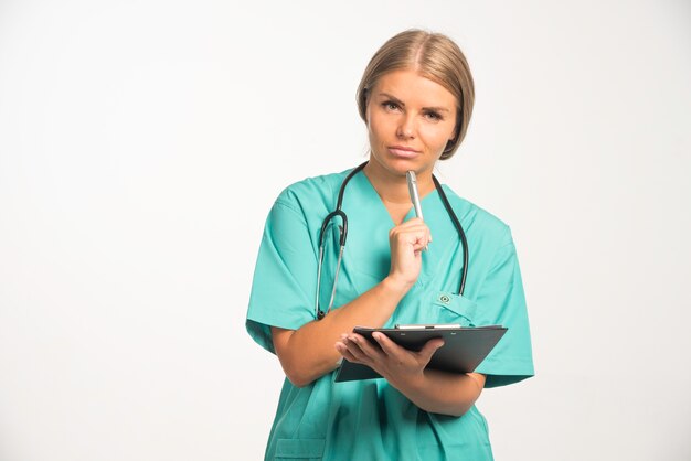 Doctora rubia en uniforme azul con estetoscopio en el cuello pensando en la historia.