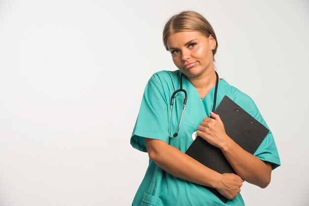 Doctora rubia en uniforme azul sosteniendo un talonario de recibos en blanco.