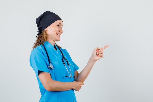 Doctora señalando con el dedo a un lado en uniforme y con aspecto alegre. .