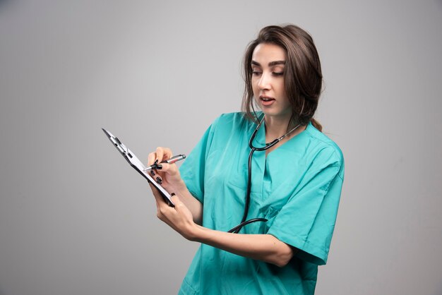 Doctora señalando notas sobre fondo gris. Foto de alta calidad