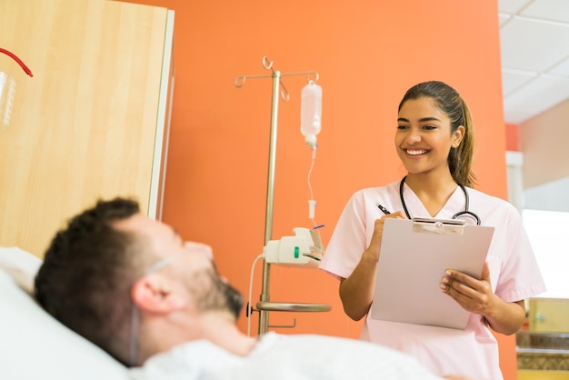 Doctora sonriente hablando con un paciente masculino mientras lee informes en el hospital