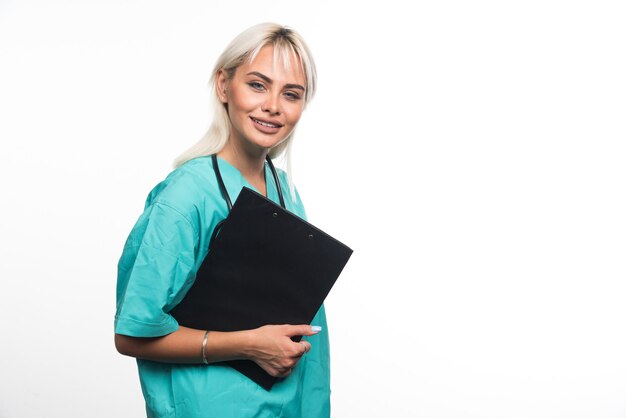 Doctora sonriente sosteniendo un portapapeles sobre superficie blanca