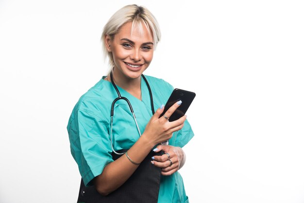 Doctora sonriente sosteniendo el portapapeles y el teléfono en la superficie blanca