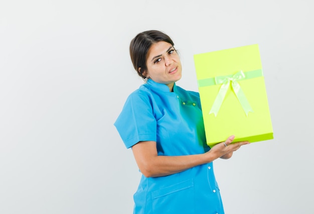 Doctora sosteniendo caja de regalo en uniforme azul y mirando confiado