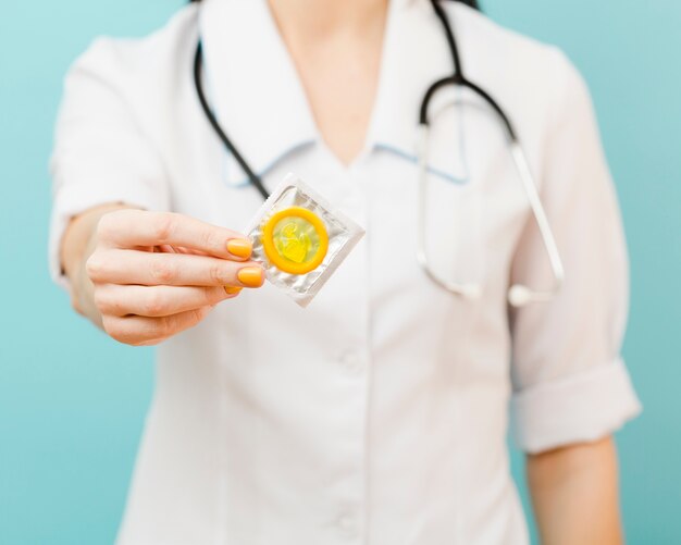 Doctora sosteniendo un condón amarillo delante de ella