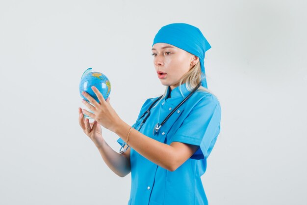 Doctora sosteniendo globo terráqueo en uniforme azul y mirando asombrado