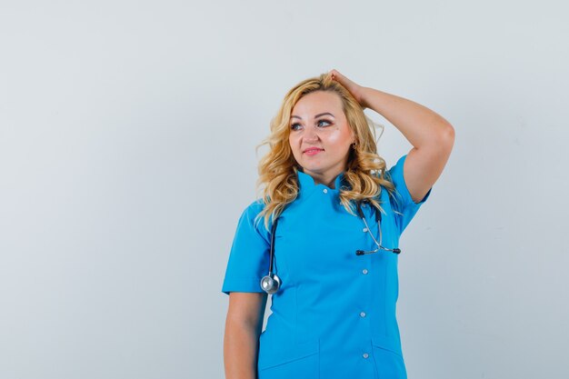 Doctora sosteniendo la mano en la cabeza en uniforme azul y luciendo optimista