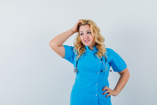 Doctora sosteniendo la mano en la cabeza en uniforme azul y mirando confiada.