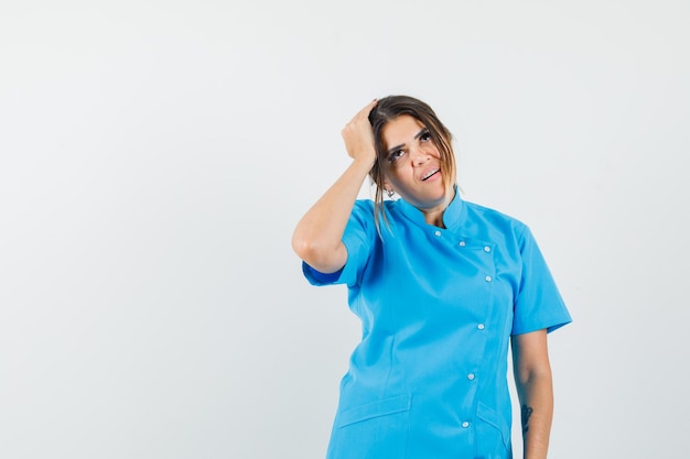 Doctora sosteniendo la mano en la cabeza en uniforme azul y mirando pensativo