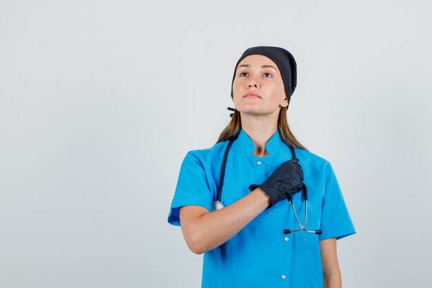 Doctora sosteniendo la mano en el estetoscopio en uniforme, guantes y mirando confiado. vista frontal.