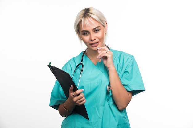 Doctora sosteniendo el portapapeles mientras piensa en la pared blanca.