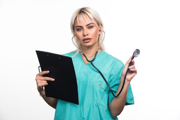 Doctora sosteniendo un portapapeles y usando un estetoscopio sobre fondo blanco. Foto de alta calidad