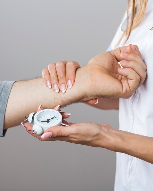 Doctora sosteniendo un reloj y una mano paciente