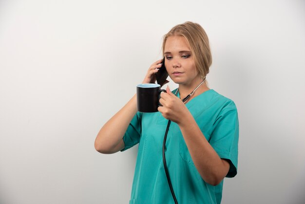 Doctora sosteniendo té mientras habla con el teléfono.