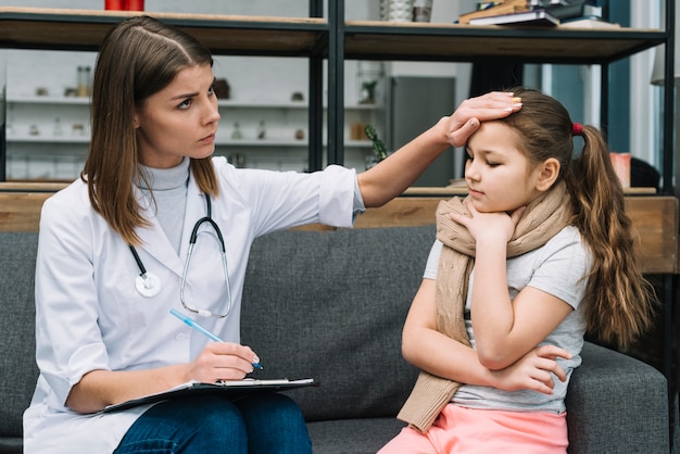 Doctora tocando la frente de la niña enferma con resfriado y fiebre.