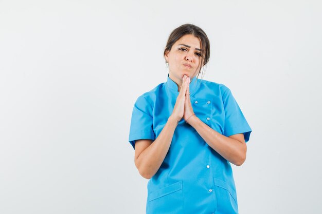 Doctora tomados de la mano en gesto de oración en uniforme azul y mirando esperanzado