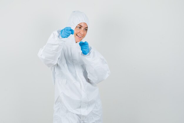 Doctora en traje de protección, guantes apuntando a la cámara y mirando alegre