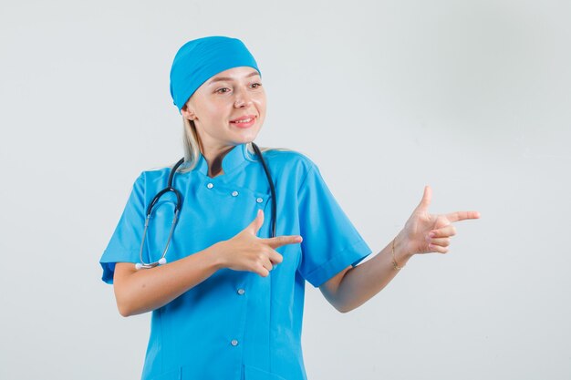 Doctora en uniforme azul apuntando al lado con gesto de pistola y mirando alegre