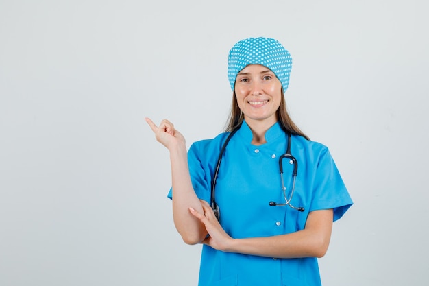 Doctora en uniforme azul apuntando con el dedo hacia atrás y mirando contento