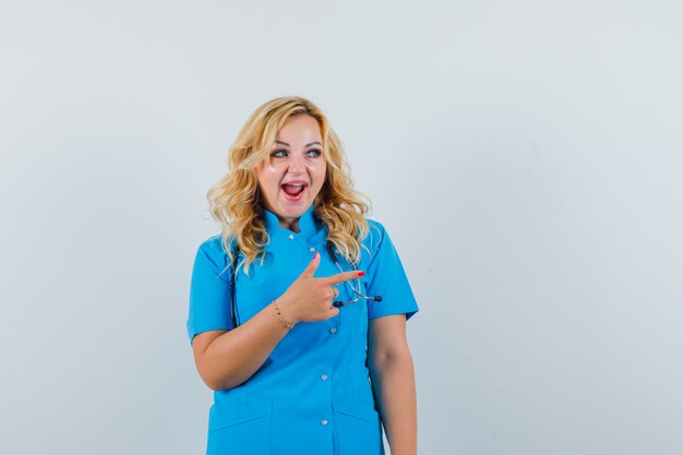 Doctora en uniforme azul apuntando a un lado y mirando alegre