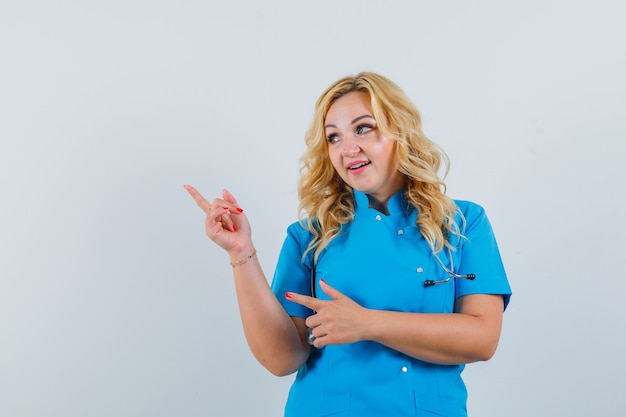 Doctora en uniforme azul apuntando a un lado y mirando complacido