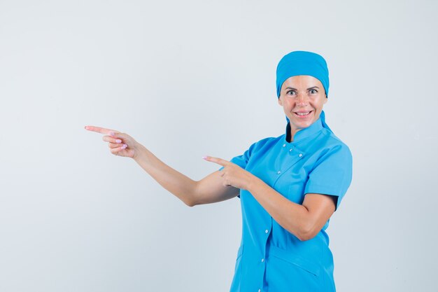 Doctora en uniforme azul apuntando hacia un lado y mirando esperanzada, vista frontal.