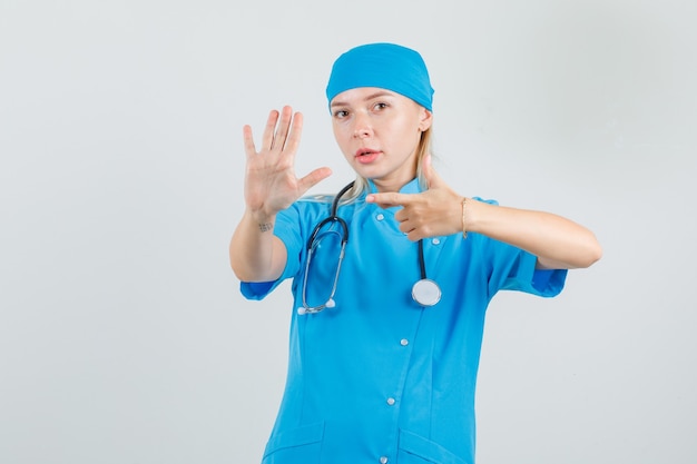 Doctora en uniforme azul apuntando a la palma de la mano levantada y mirando seria