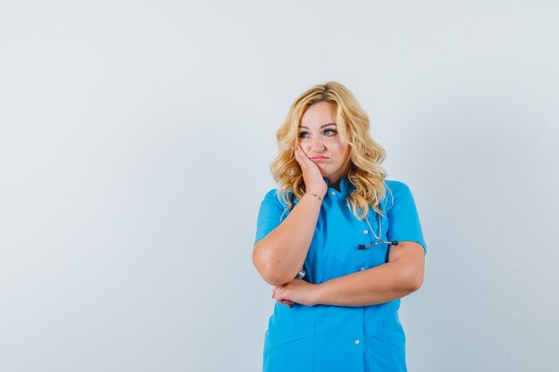 Doctora en uniforme azul centrándose a un lado y mirando infeliz espacio para texto