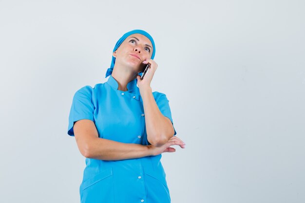 Doctora en uniforme azul hablando por teléfono móvil y mirando pensativo, vista frontal.