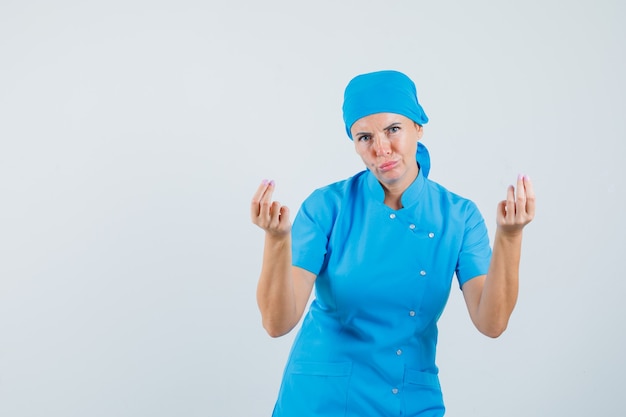 Doctora en uniforme azul haciendo gesto de dinero y mirando indigente, vista frontal.