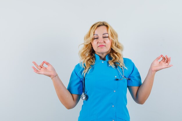 Doctora en uniforme azul haciendo meditación y mirando tranquilo