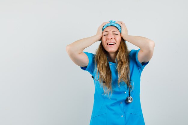 Doctora en uniforme azul juntando la cabeza con las manos y mirando arrepentido