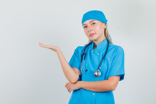 Doctora en uniforme azul manteniendo la palma levantada y sonriendo