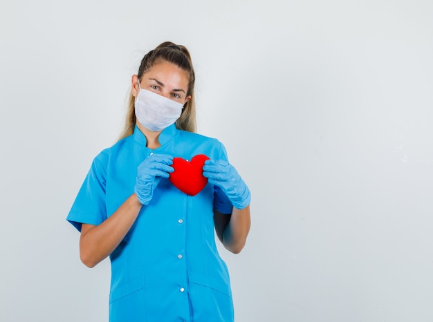 Doctora en uniforme azul, máscara, guantes con corazón rojo y aspecto optimista