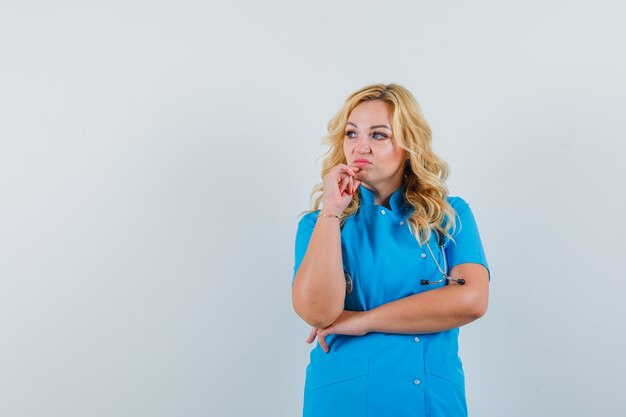 Doctora en uniforme azul mirando a un lado y mirando insatisfecho espacio para texto