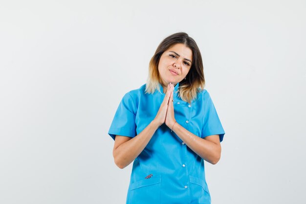 Doctora en uniforme azul mostrando gesto de namaste y mirando esperanzado