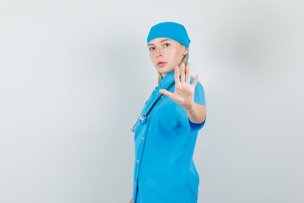 Doctora en uniforme azul mostrando gesto de rechazo con la mano y mirando serio.