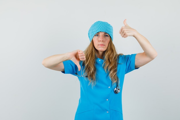 Foto gratuita doctora en uniforme azul mostrando los pulgares hacia arriba y hacia abajo