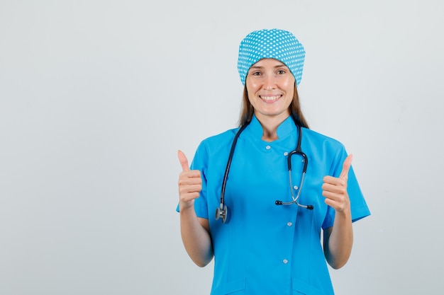 Foto gratuita doctora en uniforme azul mostrando los pulgares hacia arriba y mirando alegre