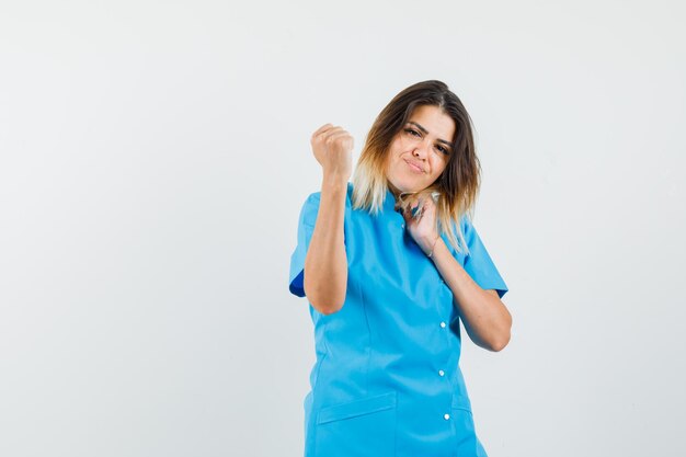 Doctora en uniforme azul mostrando el puño en alto y mirando confiado