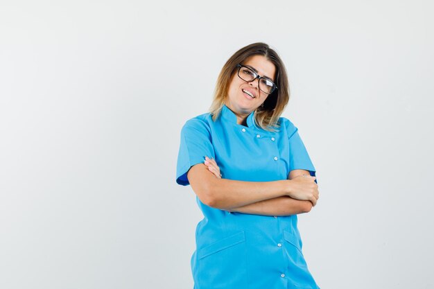 Doctora en uniforme azul de pie con los brazos cruzados y mirando alegre