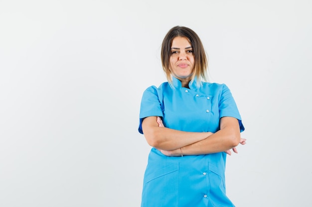 Doctora en uniforme azul de pie con los brazos cruzados y mirando confiado.