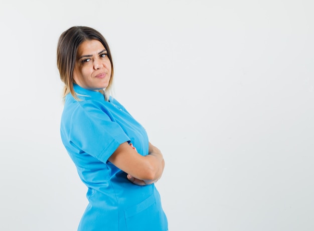 Foto gratuita doctora en uniforme azul de pie con los brazos cruzados y mirando confiado.