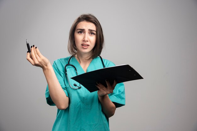 Doctora en uniforme azul con portapapeles sobre fondo gris. Foto de alta calidad