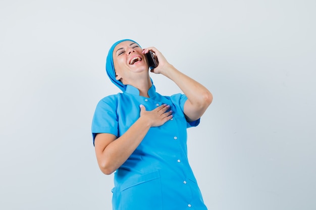 Doctora en uniforme azul riendo mientras habla por teléfono móvil, vista frontal.