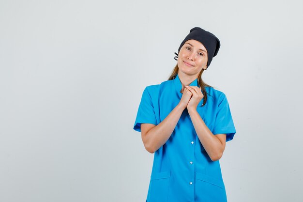 Doctora en uniforme azul, sombrero negro estrechando las manos y mirando esperanzado