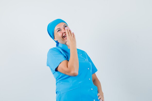 Doctora en uniforme azul sosteniendo la mano a la boca mientras se ríe, vista frontal.